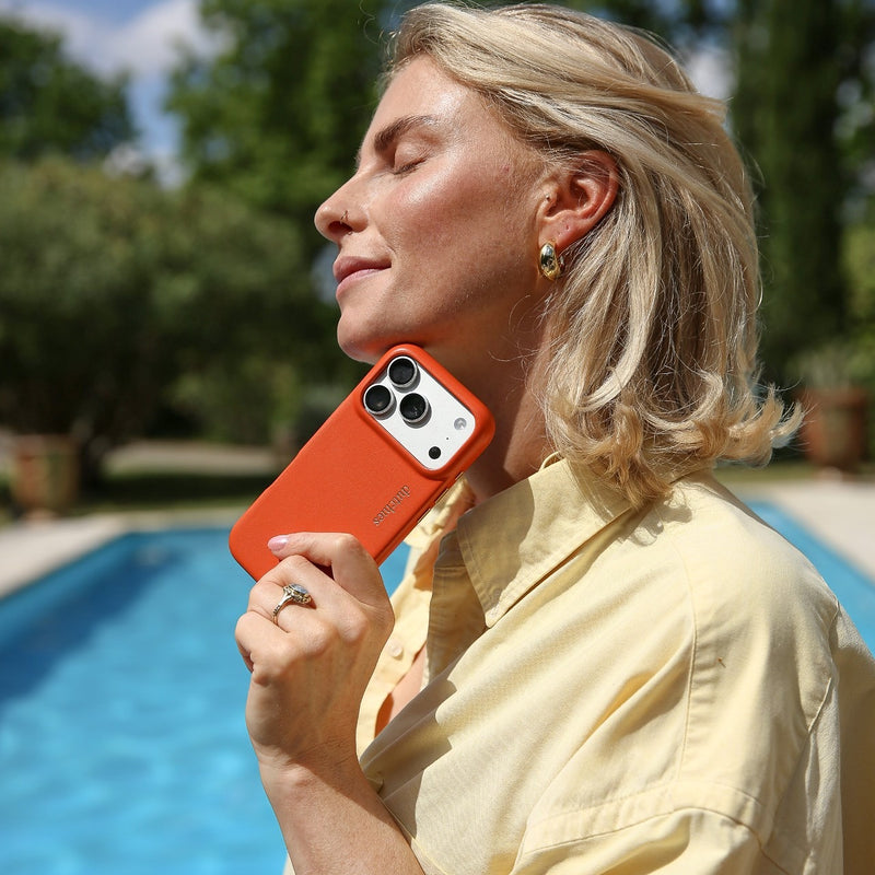 Woman enjoying the sun by the pool holding an iPhone Case | Orange (Full Wrapped) with a stylish smile.