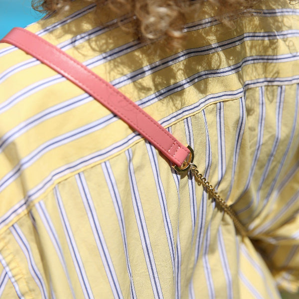 A close-up of a pink Phone Chain | Spanish | Pink attached to a trendy yellow-striped outfit.