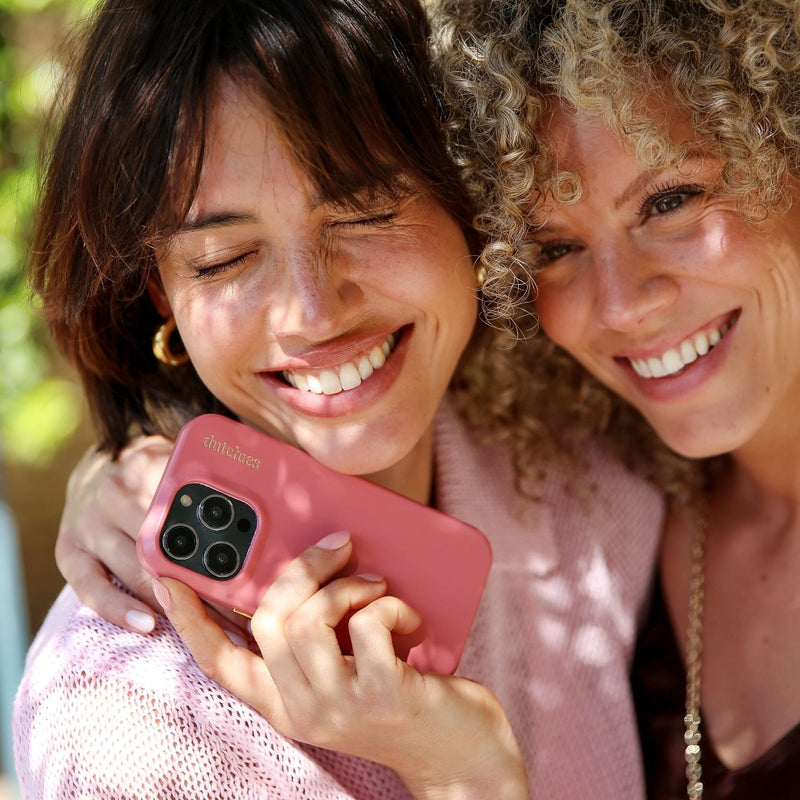 Two smiling women holding an iPhone Case | Pink (Full Wrapped) in a sunny outdoor setting.