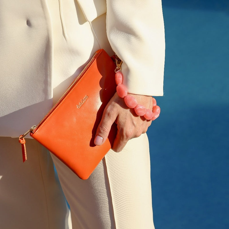 Toiletry Bag | Orange held stylishly with a pink accessory, perfect for summer vacations and beach trips.