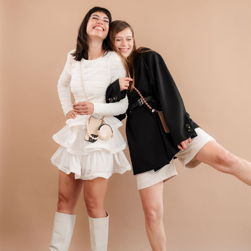 Zwei Frauen posieren in stilvollen Outfits und präsentieren die Beaded Phone Chain Kollektion vor einem neutralen Hintergrund.