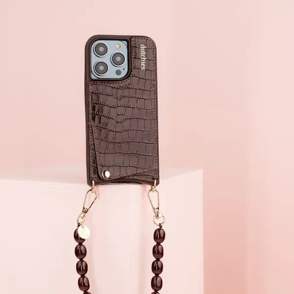 Phone case with crocodile texture and beaded strap on a pink background