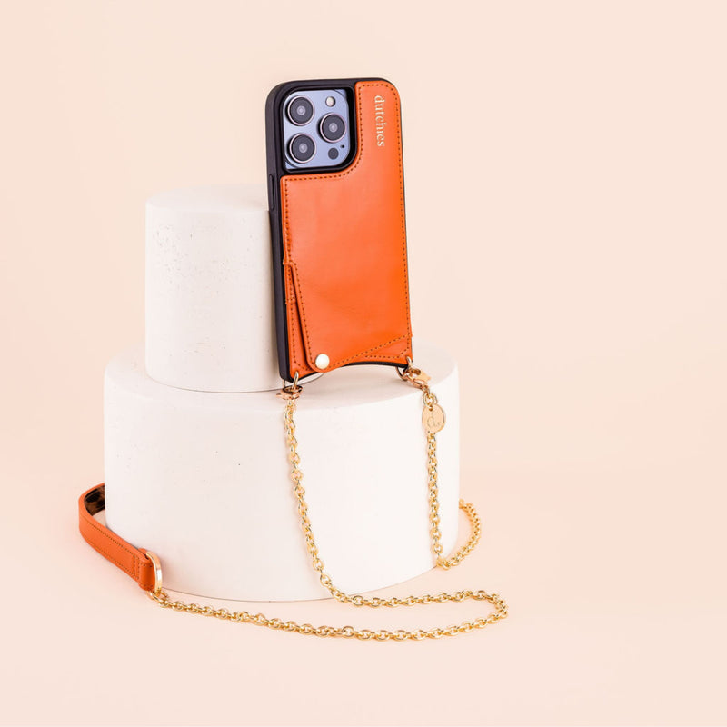 Spanish Kettenset | iPhone | Orange elegant auf einem Marmorpodest präsentiert und zeigt die schicke Handyhülle und Kette.