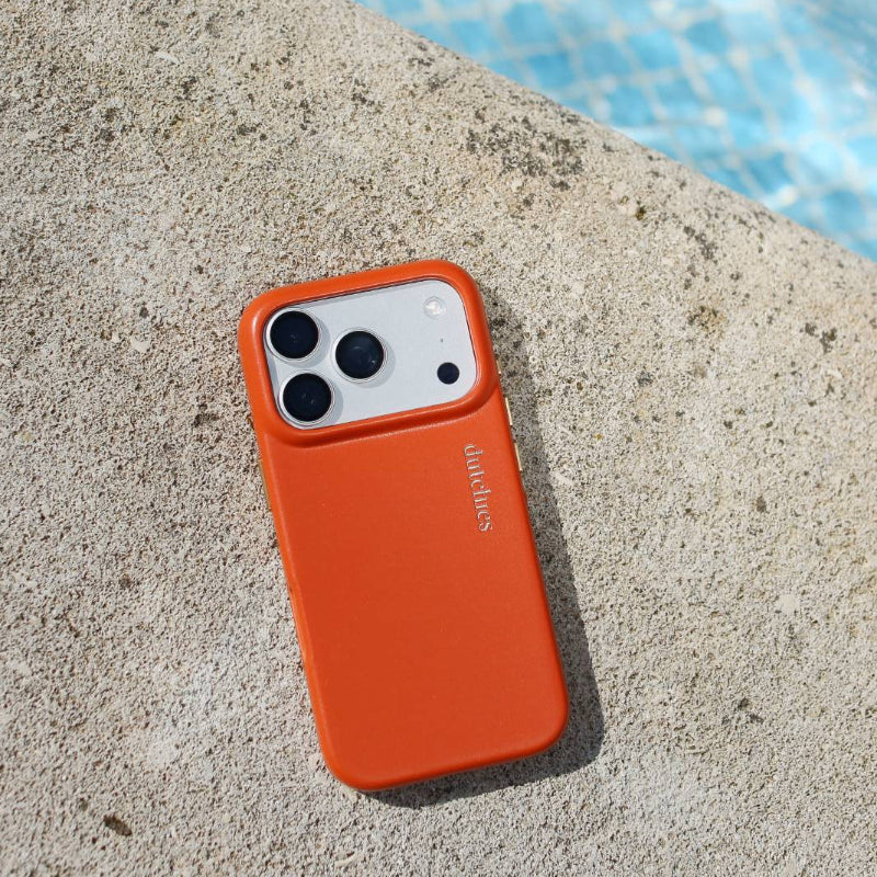 iPhone Hülle | Orange (Full Wrapped) liegt auf einer Steinoberfläche am Pool und zeigt ihr minimalistisches Design und das hochwertige Leder.