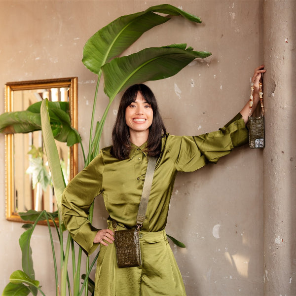 Model showcasing the Phone Bag Juliet | Olive Green with stylish outfit and plants in background.