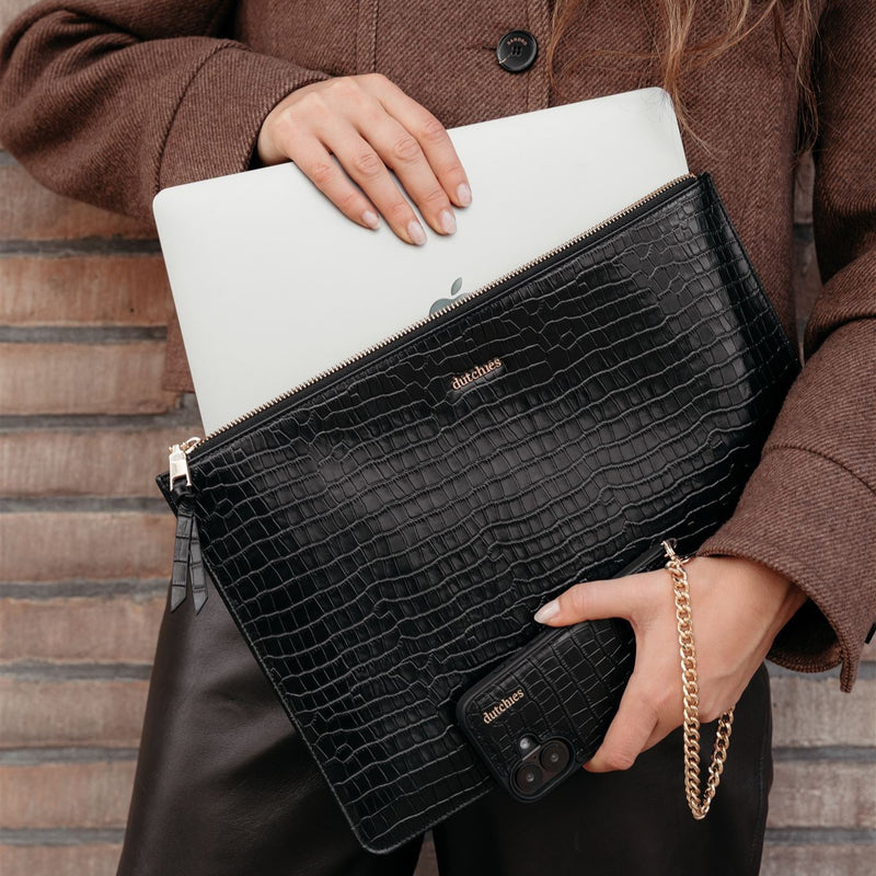 Stilvolle schwarze Laptophülle mit Krokodilmuster, die einen Laptop schützt und von einer Frau mit passender Handyhülle gehalten wird.