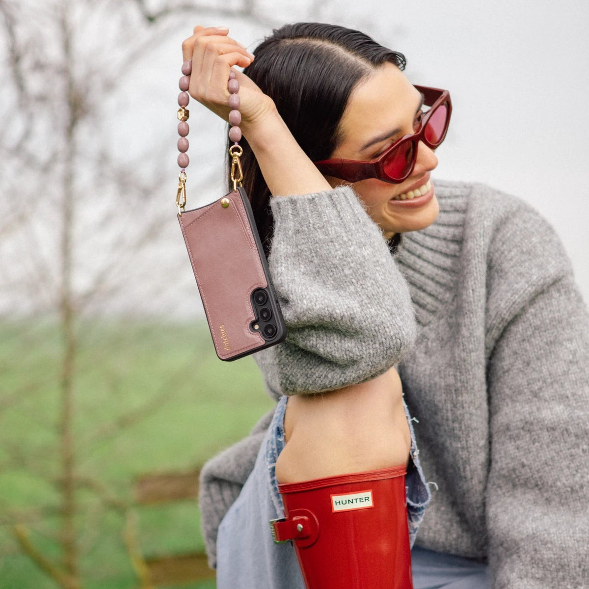 Samsung-Hülle | Mauve, gehalten von einer Frau in stilvollem grauen Pullover und Sonnenbrille, die das schicke Design und das Kartenfach zeigt.