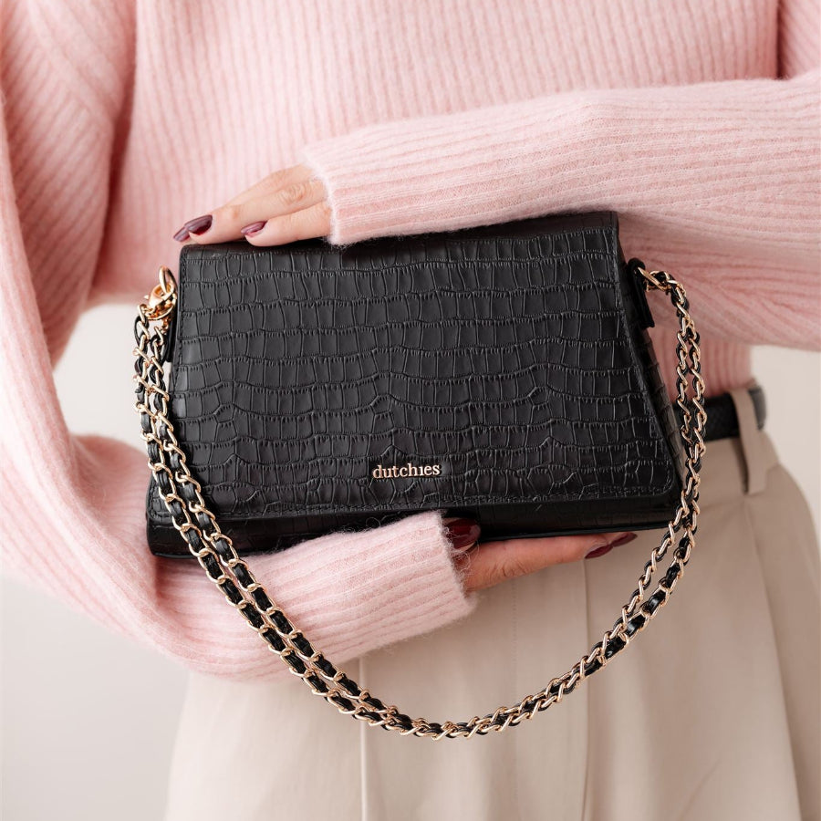Sophie Crossbody Bag | Noir Gold holdt af en stilfuld kvinde iført en pink sweater, der fremviser dens elegance og praktiske anvendelighed.
