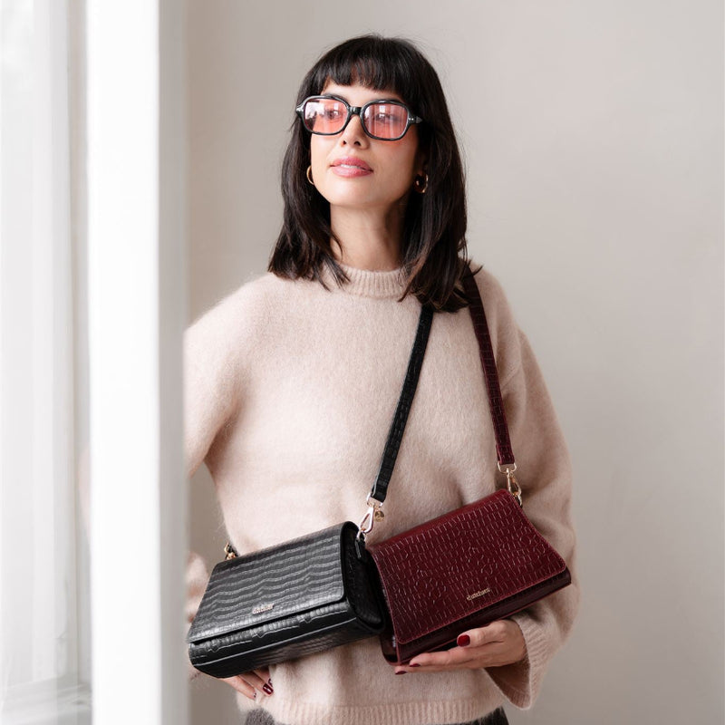 Modella di stile che mostra Sophie Crossbody Bag | Noir Gold con altre borse, perfetta borsa per telefono per ogni occasione.