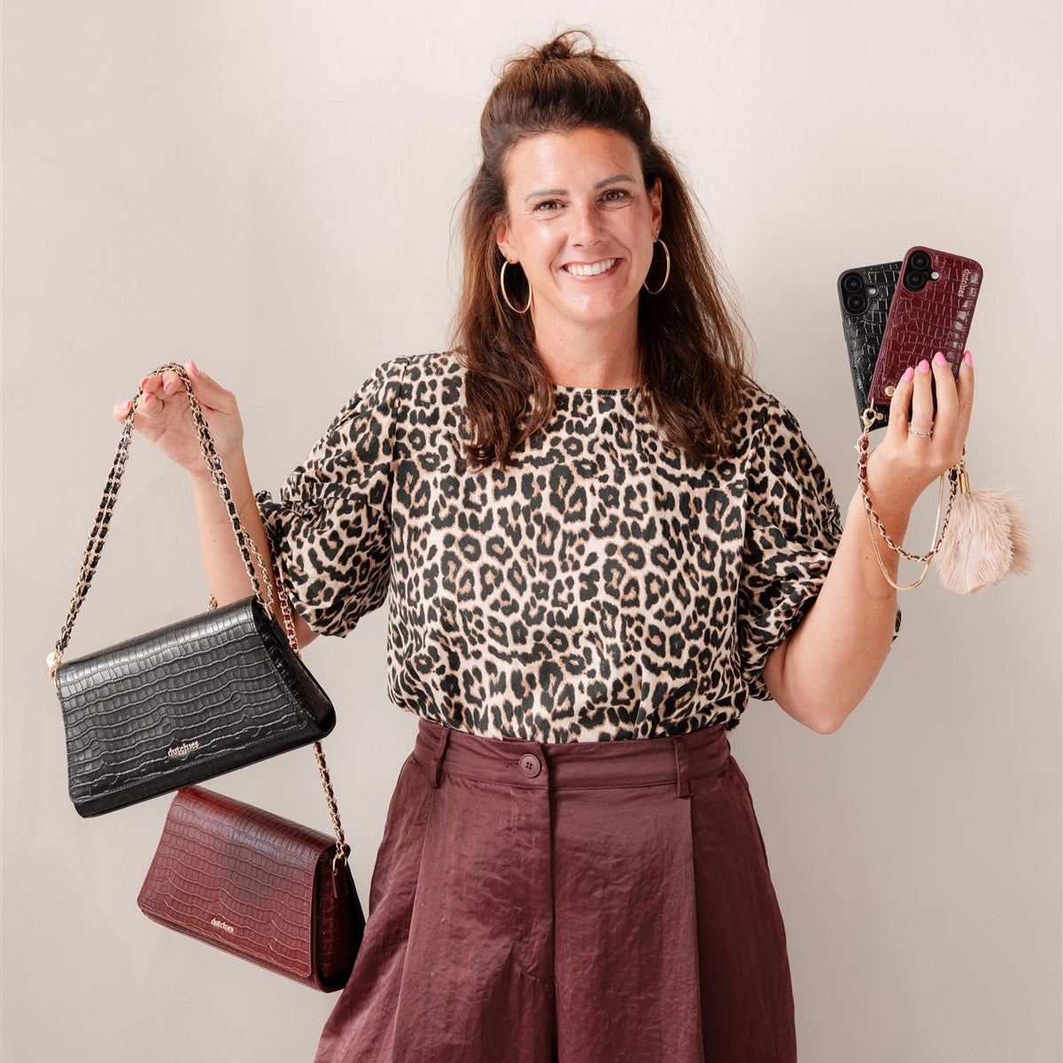 Smilende kvinde, der viser Sophie Crossbody Bag | Noir Gold, stilfulde telefonposer og trendy tøj.