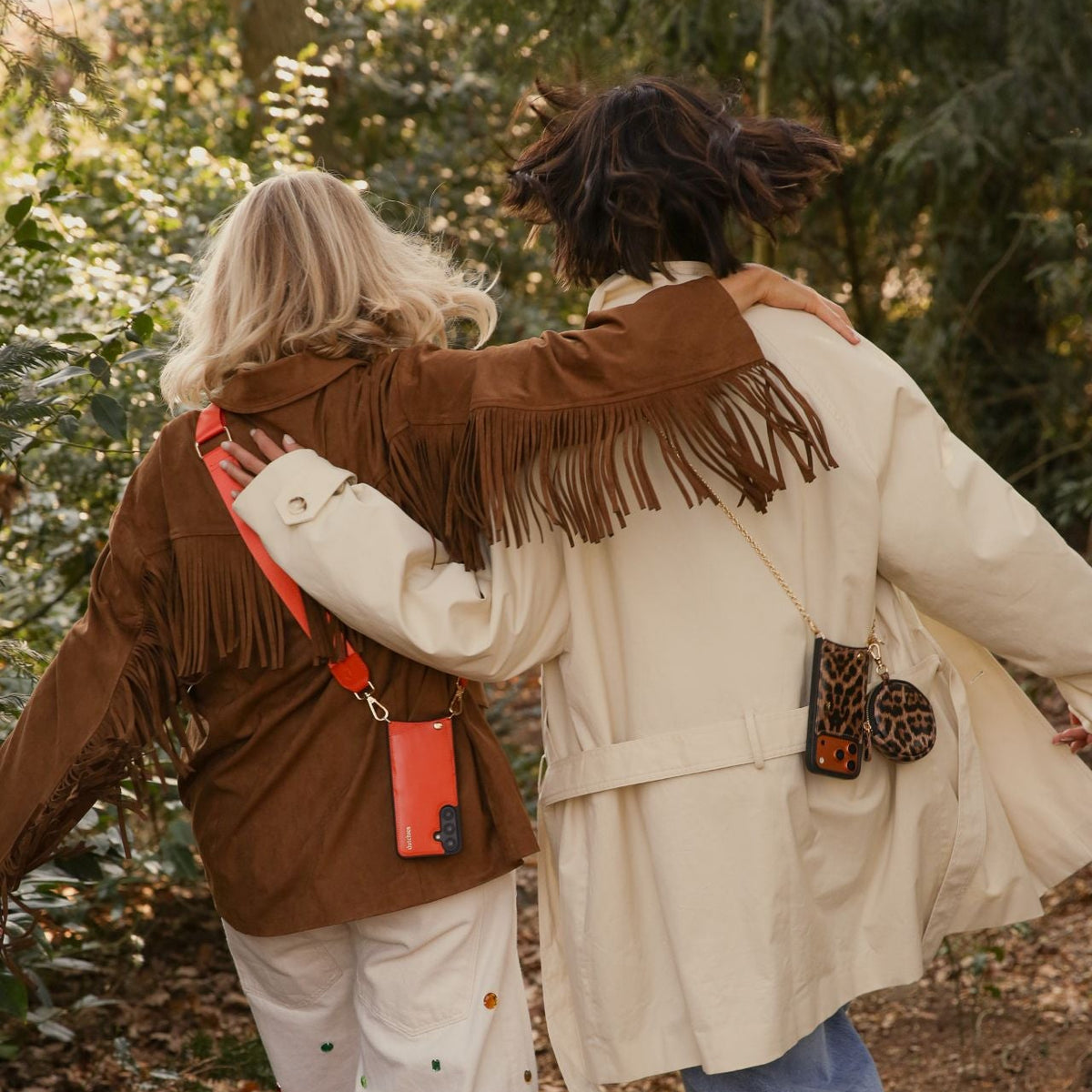 Two friends wearing fringe jackets, showcasing the Mini Phone Bag Emma | Leopard in a forest setting.