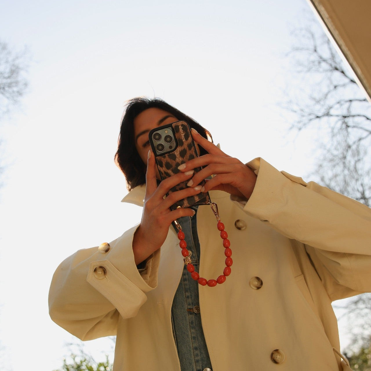 A person holding a phone with a Tamara phone charm, showcasing its vibrant orange beaded design.